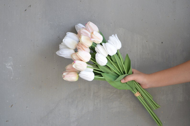 May include: A bouquet of artificial tulips in shades of white and pink. The tulips are arranged in a hand holding the stems.