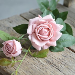 Op de afbeelding: Twee roze kunstmatige rozen met groene bladeren op een houten oppervlak.