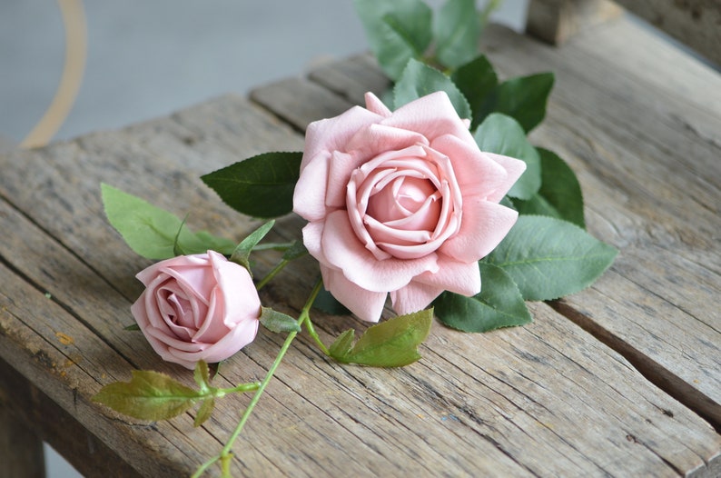 Op de afbeelding: Twee roze kunstmatige rozen met groene bladeren op een houten oppervlak.