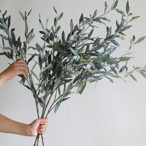 May include: A bunch of artificial olive branches with green leaves and small brown and green olives.