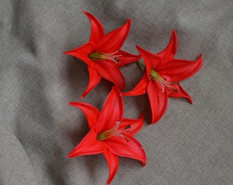 May include: Three red artificial lilies with green centers on a gray textured background.