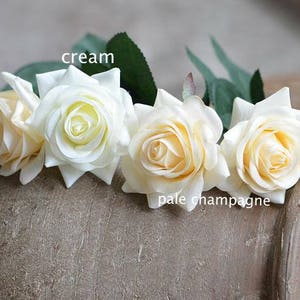 May include: Four artificial roses in a cream and pale champagne color. The roses are arranged in a circle, with the cream roses on the left and right and the pale champagne roses in the center.