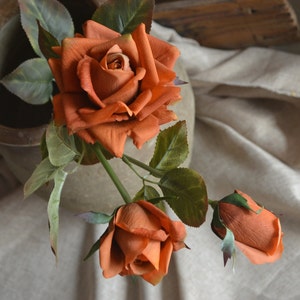 May include: Three artificial orange roses with green leaves. The roses are arranged in a bouquet.
