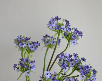 May include: A bouquet of purple and green artificial flowers with delicate blooms. The flowers are arranged in a cluster and have a natural, realistic appearance.