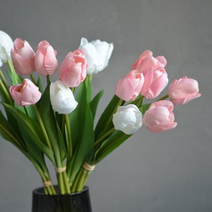 May include: A bouquet of pink and white artificial tulips in a clear glass vase. The tulips are arranged in a vase on a gray background.