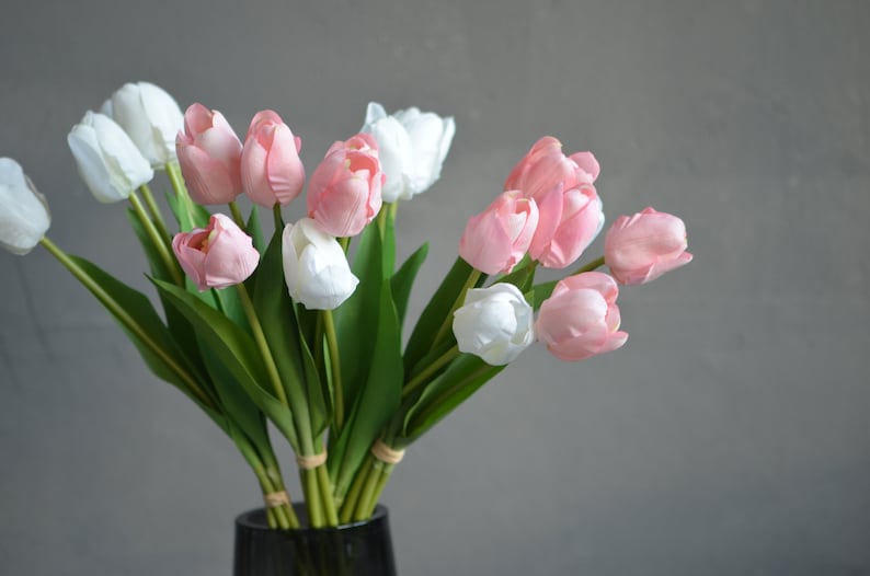 May include: A bouquet of pink and white artificial tulips in a clear glass vase. The tulips are arranged in a vase on a gray background.