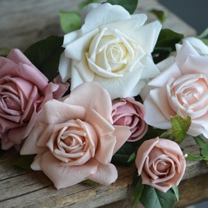 Op de afbeelding: Een boeket van kunstmatige rozen in tinten roze en wit. De rozen zijn in een tros gerangschikt, met de witte roos in het midden. De rozen zijn gemaakt van een zacht, zijdeachtig materiaal en hebben een realistisch uiterlijk.