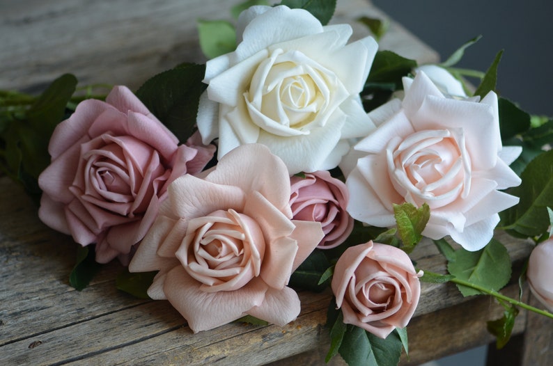 Op de afbeelding: Een boeket van kunstmatige rozen in tinten roze en wit. De rozen zijn in een tros gerangschikt, met de witte roos in het midden. De rozen zijn gemaakt van een zacht, zijdeachtig materiaal en hebben een realistisch uiterlijk.