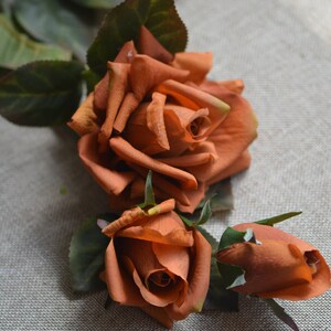 May include: Three artificial orange roses with green leaves. The roses are arranged in a bouquet.