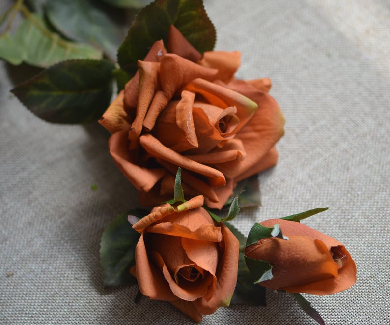 May include: Three artificial orange roses with green leaves. The roses are arranged in a bouquet.
