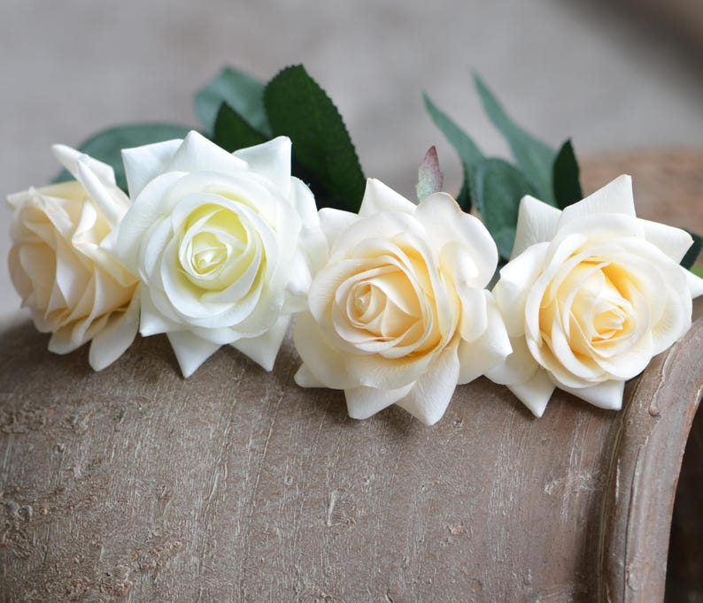 May include: Four cream-colored artificial roses with green stems and leaves.