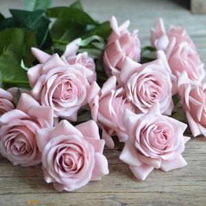 May include: A bouquet of pale pink artificial roses with green leaves on a rustic wooden surface.