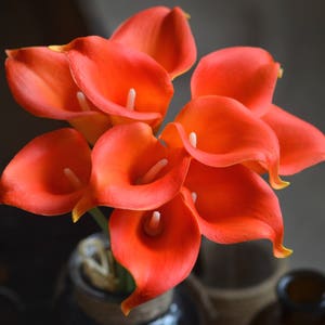 May include: A bouquet of orange calla lilies. The flowers are arranged in a vase and are in full bloom.