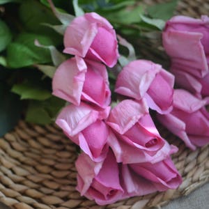 May include: A bouquet of pink artificial roses arranged on a woven wicker surface. The roses are made of fabric and have a realistic appearance.