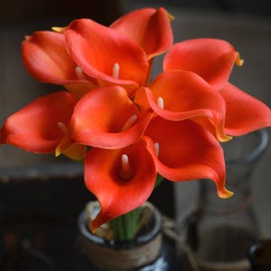 May include: A bouquet of orange calla lilies arranged in a vase. The lilies are in full bloom and have a delicate, elegant appearance.