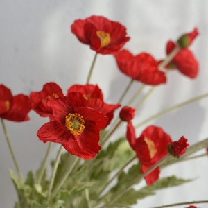 May include: A bouquet of red silk poppy flowers with green stems and leaves. The flowers have a yellow center.