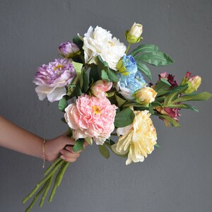 May include: A bouquet of artificial flowers in various colors, including pink, white, blue, and purple. The flowers are arranged in a loose, natural style and have a realistic appearance.