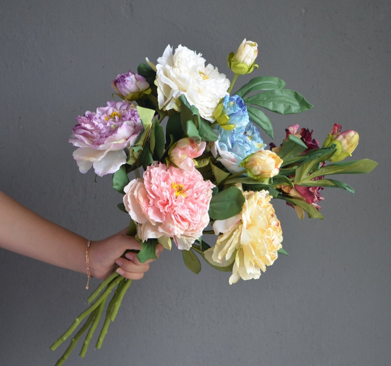 May include: A bouquet of artificial flowers in various colors, including pink, white, blue, and purple. The flowers are arranged in a loose, natural style and have a realistic appearance.