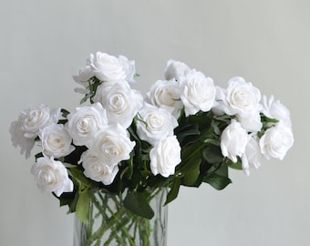 May include: A bouquet of white silk roses in a clear glass vase. The roses are arranged in a cluster, with the stems extending out of the vase.
