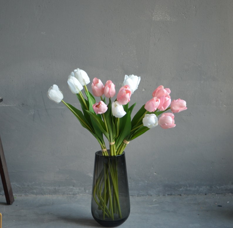 May include: A bouquet of pink and white tulips in a gray vase. The tulips are arranged in a vase with a narrow neck and a wide base.