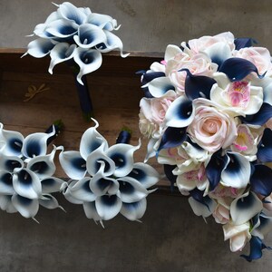May include: A bridal bouquet with white and navy blue calla lilies, pink roses, and white orchids. The bouquet is arranged in a cascading style and is surrounded by smaller bouquets of white and navy blue calla lilies.