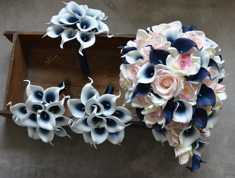 May include: A bridal bouquet with white and navy blue calla lilies, pink roses, and white orchids. The bouquet is arranged in a cascading style and is surrounded by smaller bouquets of white and navy blue calla lilies.