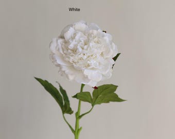 May include: A single white artificial peony flower with green leaves. The flower is in bloom and has a delicate, ruffled texture. The stem is green and has a few leaves.