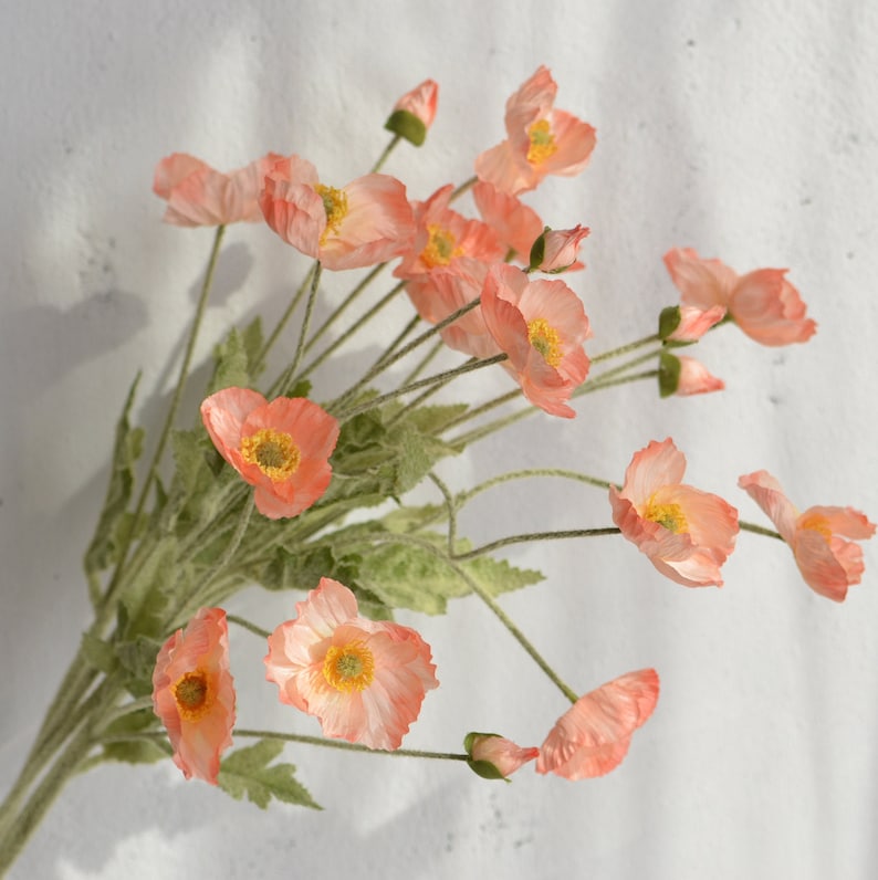 May include: A bouquet of peach-colored artificial poppy flowers with green stems and leaves.