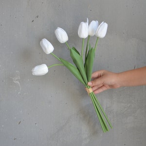 May include: A bouquet of white tulips with green stems tied together with a gold ribbon.
