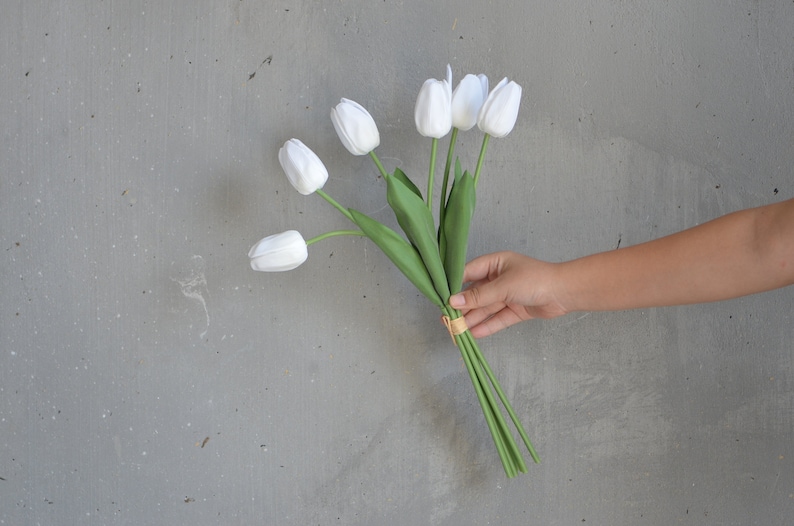 May include: A bouquet of white tulips with green stems tied together with a gold ribbon.