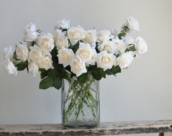 Peut inclure: Un bouquet de roses blanches disposé dans un vase en verre transparent. Le vase est posé sur une surface en bois rustique.
