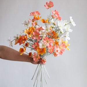 Könnte beinhalten: Ein Strauß künstlicher Blumen in Orange-, Weiß- und Rosatönen. Die Blumen sind in einem lockeren, natürlichen Stil angeordnet und haben eine zarte, feminine Ausstrahlung.