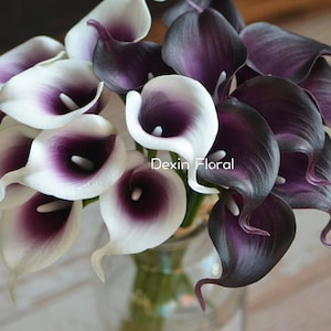 Puede incluir: Un ramo de lirios artificiales de cala con pétalos blancos y centros morados. El ramo incluye lirios de cala de color morado oscuro y blanco.