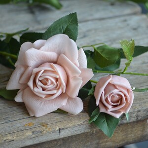 Op de afbeelding: Twee roze kunstbloemen met groene bladeren op een rustiek houten oppervlak.