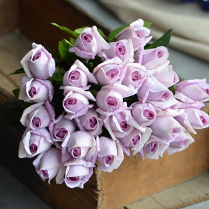 May include: A bouquet of lavender-colored silk roses arranged in a wooden box. The roses are tightly packed together, creating a full and lush look.