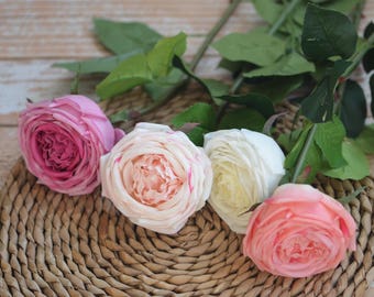 May include: Four artificial roses in different shades of pink, peach, and white. The roses are arranged on a woven wicker surface.