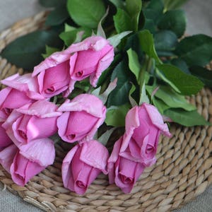 May include: A bouquet of pink artificial roses with green leaves. The roses are arranged in a cluster and have a realistic appearance.
