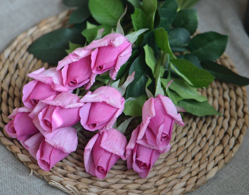 May include: A bouquet of pink artificial roses with green leaves. The roses are arranged in a cluster and have a realistic appearance.