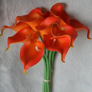 May include: A bouquet of orange calla lilies with green stems. The flowers are arranged in a cluster, with the stems tied together at the base.