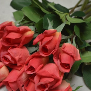 Puede incluir: Un ramo de rosas rojas artificiales con hojas verdes. Las rosas est&aacute;n dispuestas en un racimo, con los tallos visibles.