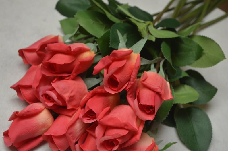 Puede incluir: Un ramo de rosas rojas artificiales con hojas verdes. Las rosas est&aacute;n dispuestas en un racimo, con los tallos visibles.