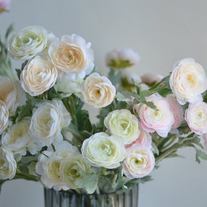 May include: A bouquet of artificial flowers in shades of white and pink. The flowers have a delicate, layered appearance and are arranged in a vase.