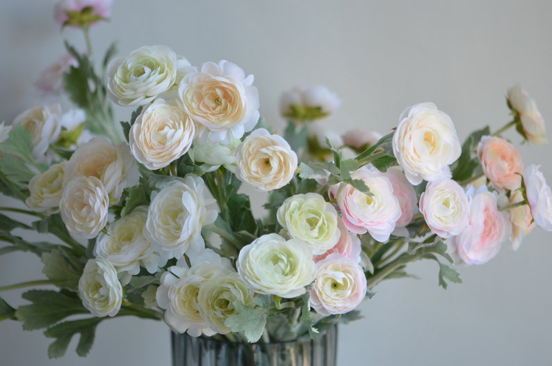 May include: A bouquet of artificial flowers in shades of white and pink. The flowers have a delicate, layered appearance and are arranged in a vase.