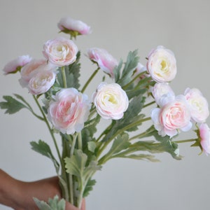 May include: A bouquet of pink and white artificial ranunculus flowers with green leaves.
