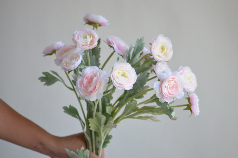 May include: A bouquet of pink and white artificial ranunculus flowers with green leaves.