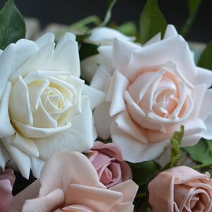 Op de afbeelding: Een boeket kunstmatige rozen in tinten wit, roze en blush. De rozen zijn in een cluster gerangschikt, met de witte rozen in het midden en de roze rozen eromheen.