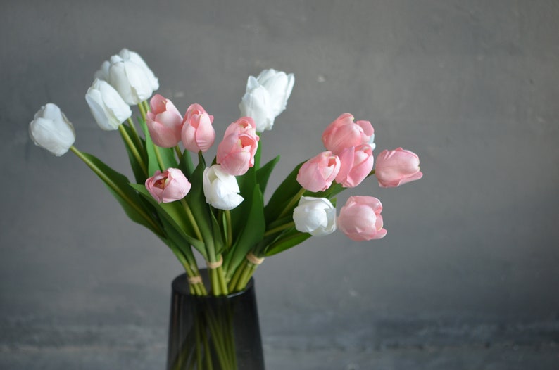 May include: A bouquet of pink and white artificial tulips in a gray vase. The tulips are arranged in a vase on a gray background.