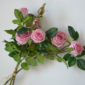 May include: A bouquet of pink artificial roses with green leaves and stems. The roses are arranged in a loose, natural style.