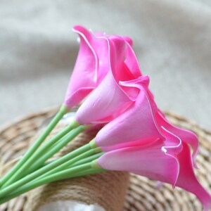 Puede incluir: Un ramo de vibrantes calas rosas con bordes blancos y tallos verdes. Las flores est&aacute;n dispuestas sobre una base de mimbre tejido, creando una exhibici&oacute;n natural y elegante. Los lirios son un acento brillante y llamativo.