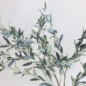 May include: A sprig of artificial olive branches with green leaves and small dark purple olives.